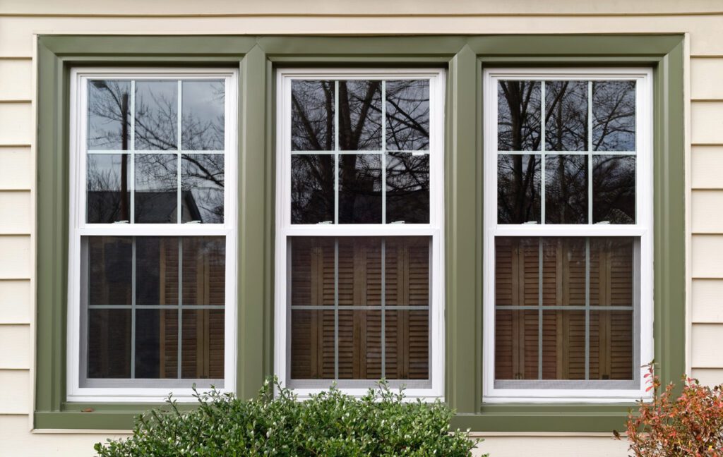 Three new replacement windows with green trim on front of house. Horizontal. New windows and doors can lower the energy costs for your PA or NJ home.