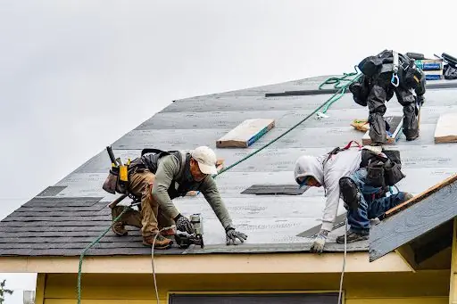 KPI roofing crew installing asphalt shingles on a house roof.