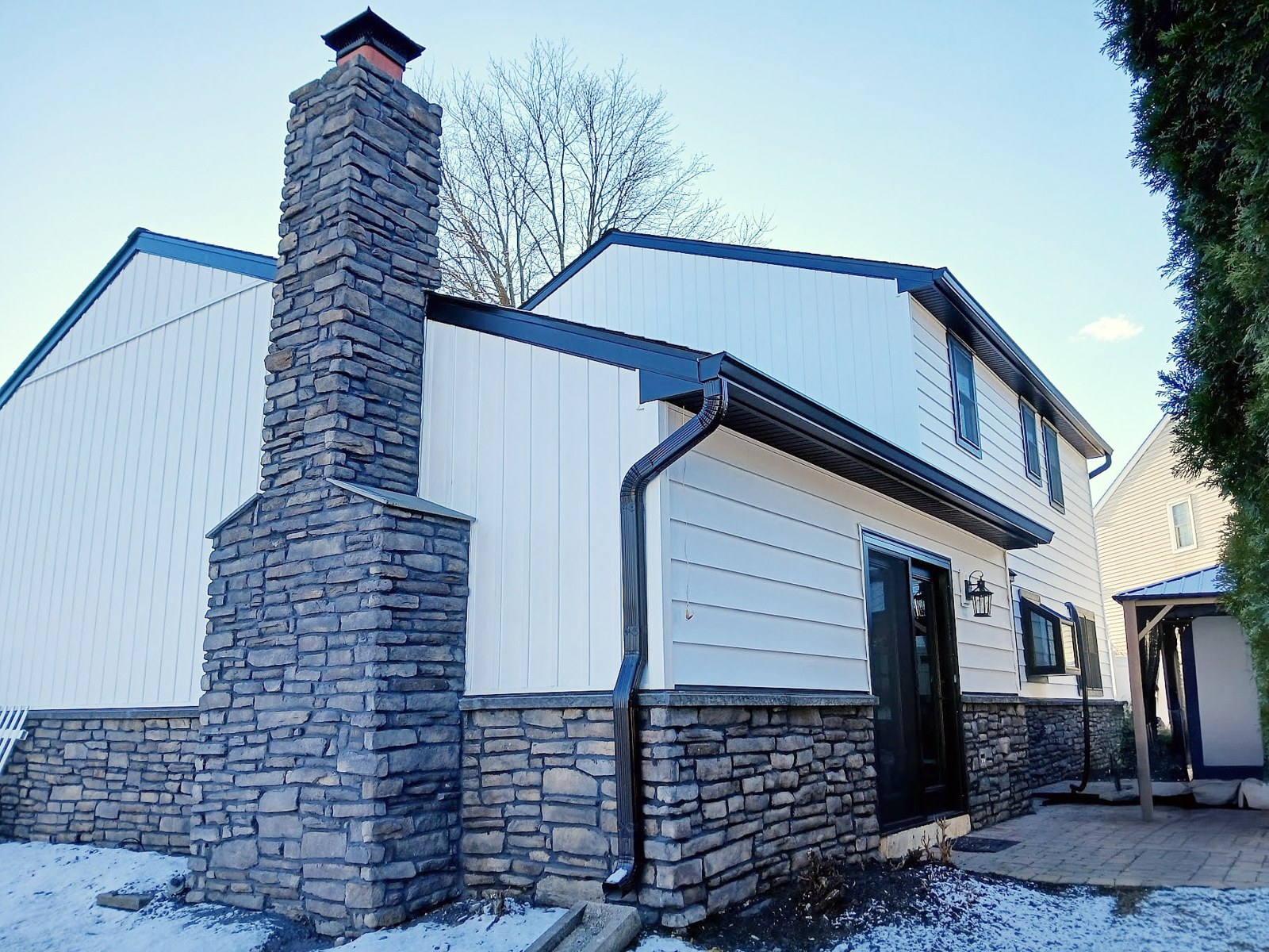 New dark gutters and a downspout on a white and stone home, with snow on the ground